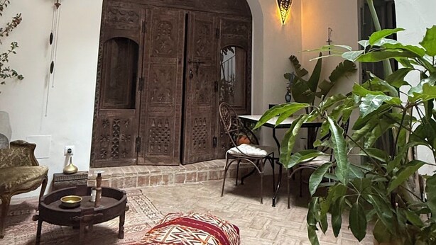 Un patio con techo de madera, un gran arco de entrada, una mesa con sillas y una planta en maceta.