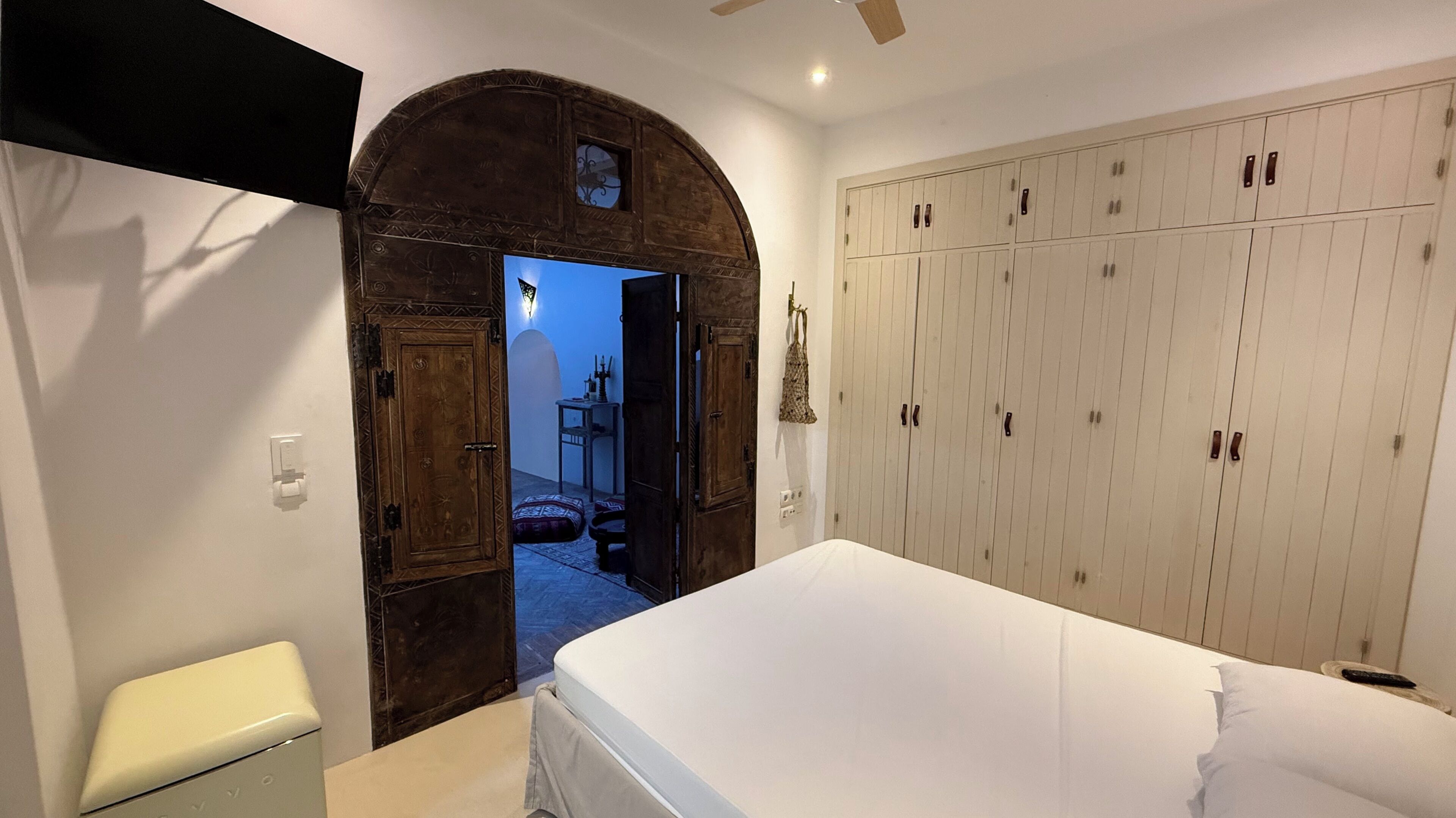 Quarto com um guarda-roupa espaçoso, uma cama e uma porta arqueada que dá para uma varanda.