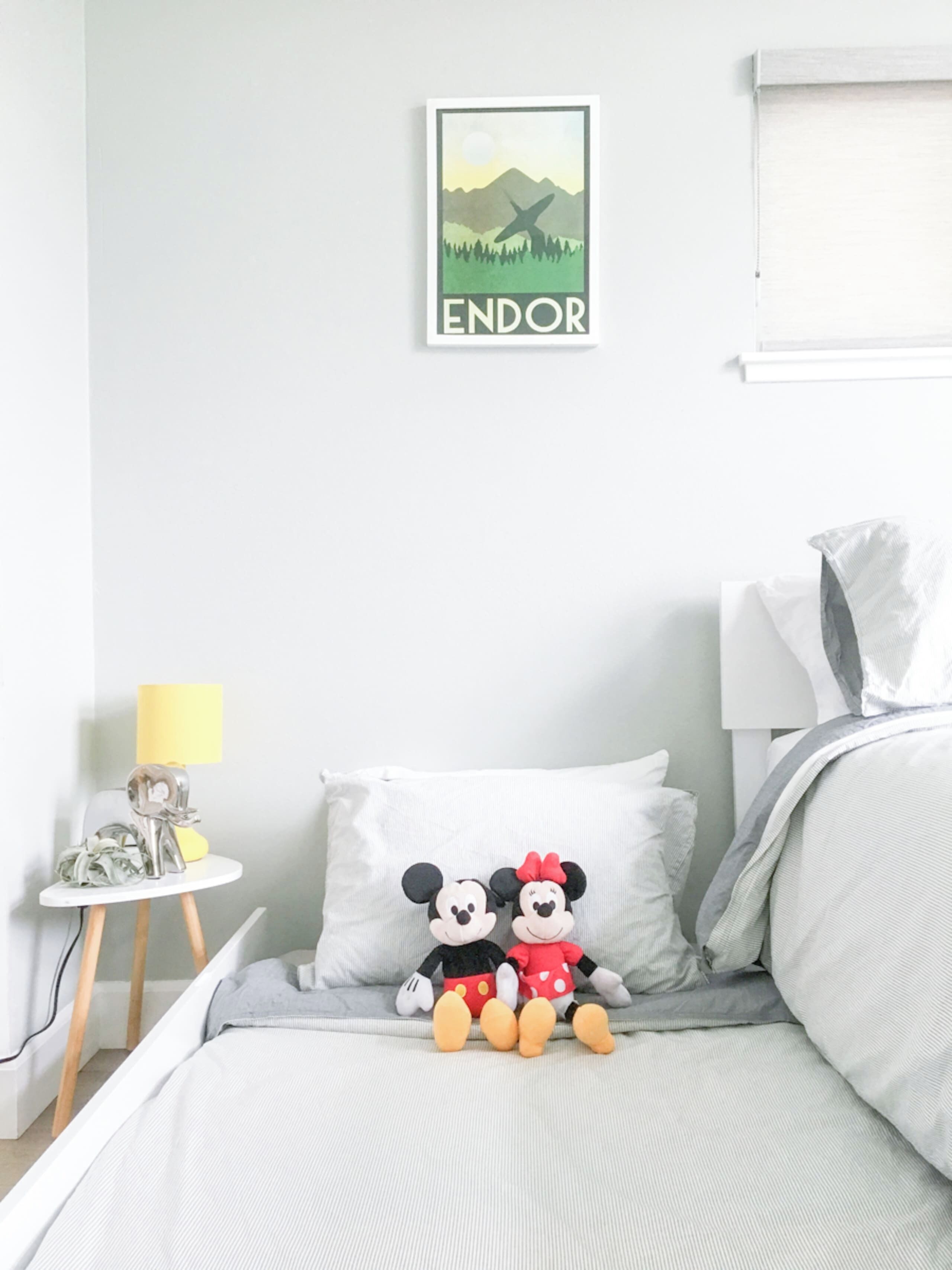 Ein Schlafzimmer mit Bett, Kissen, einem kleinen Tisch mit Lampe und einem Wandbild.