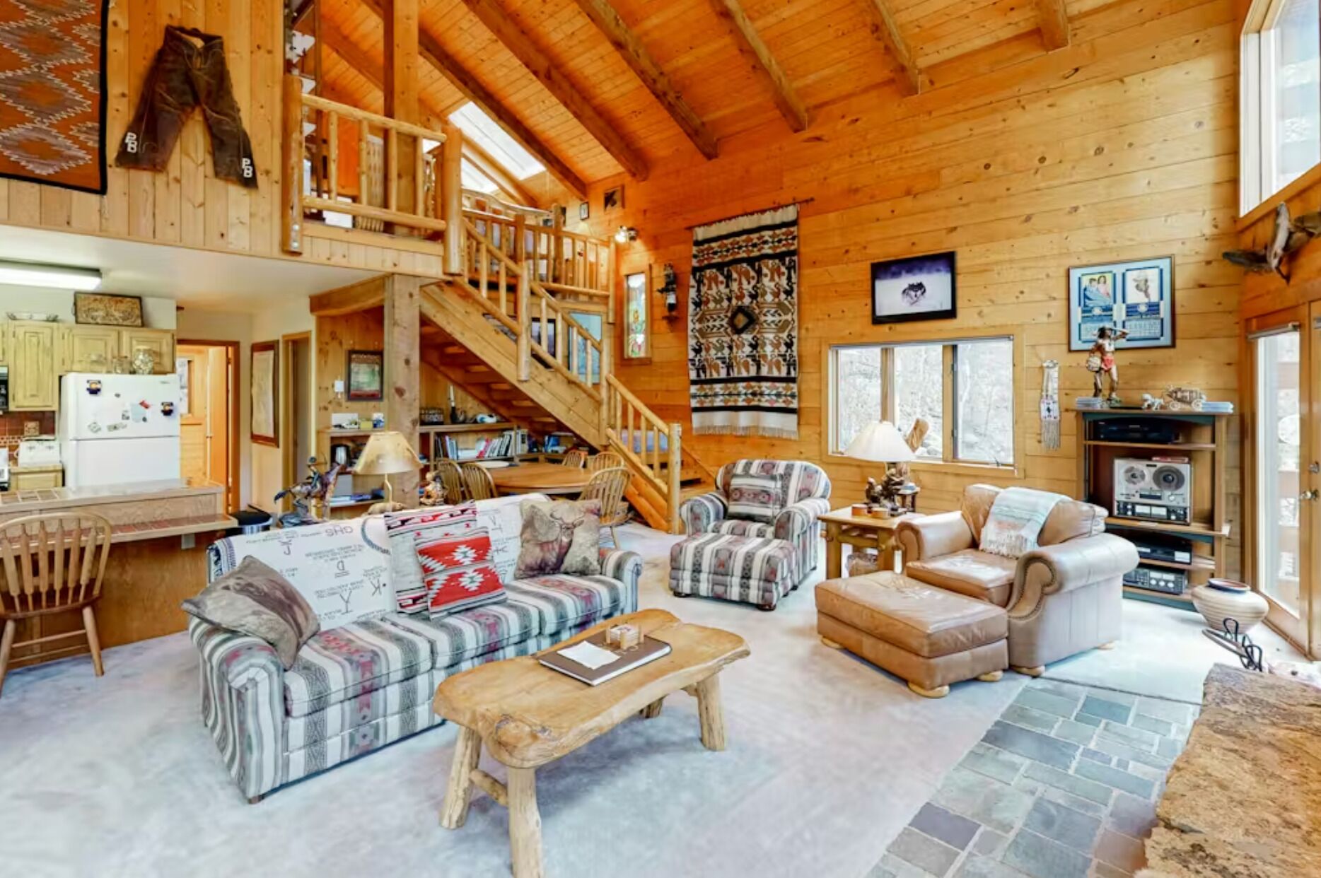 A log cabin interior with a living room, kitchen, and a staircase leading to an upper level.