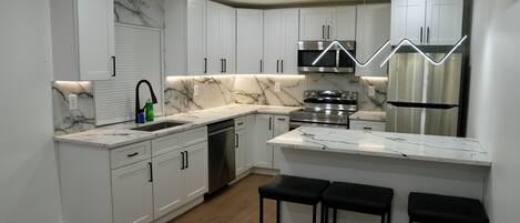 A modern kitchen with white cabinetry, a marble countertop, stainless steel appliances, and a central island with bar stools.