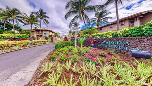 Ein privater Zufahrtsweg mit einem Schild für Waikoloa Colony Villas, umgeben von üppiger tropischer Vegetation und Palmen.