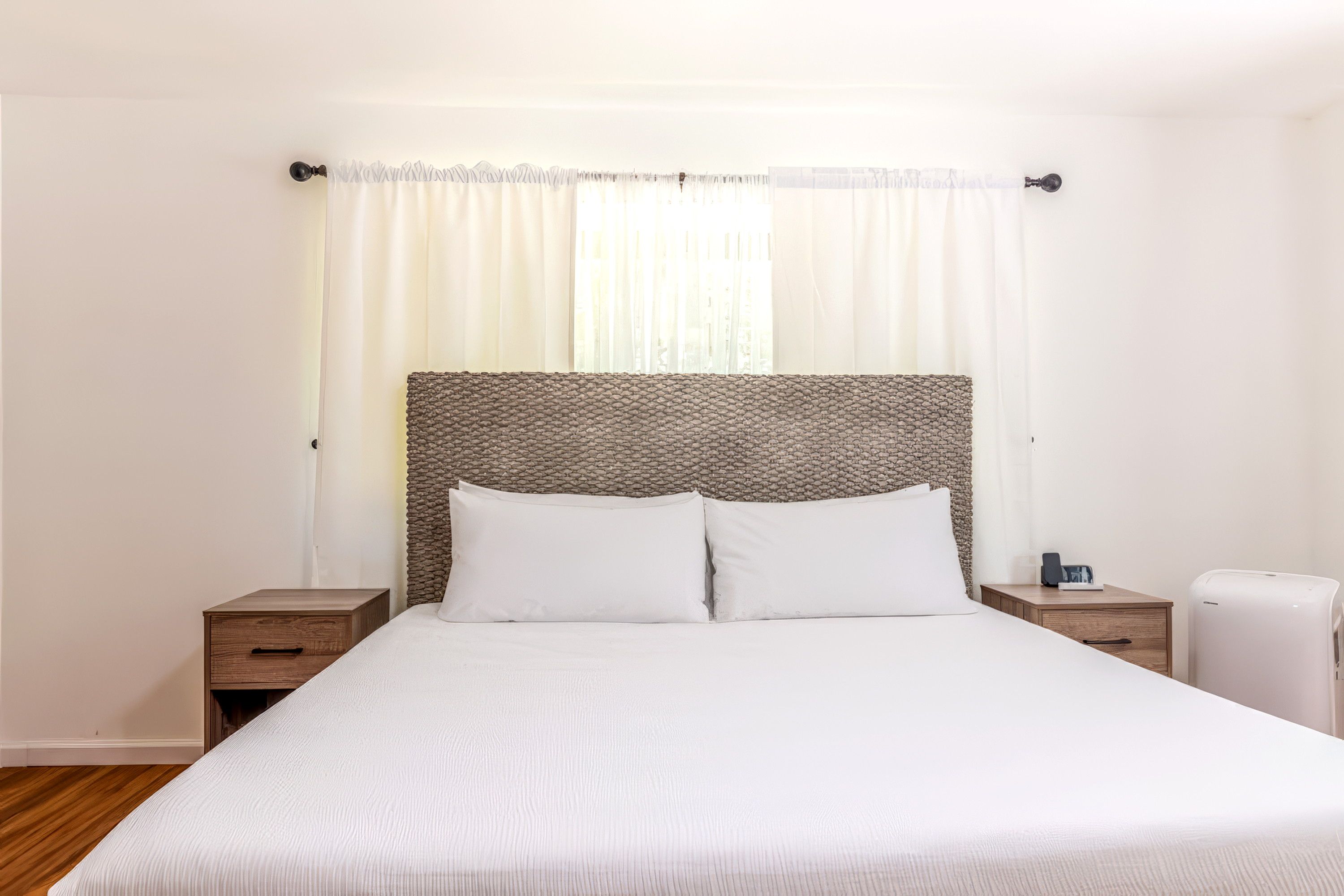 A hotel room with a bed, two bedside tables, a nightstand, a lamp, and a white radiator.