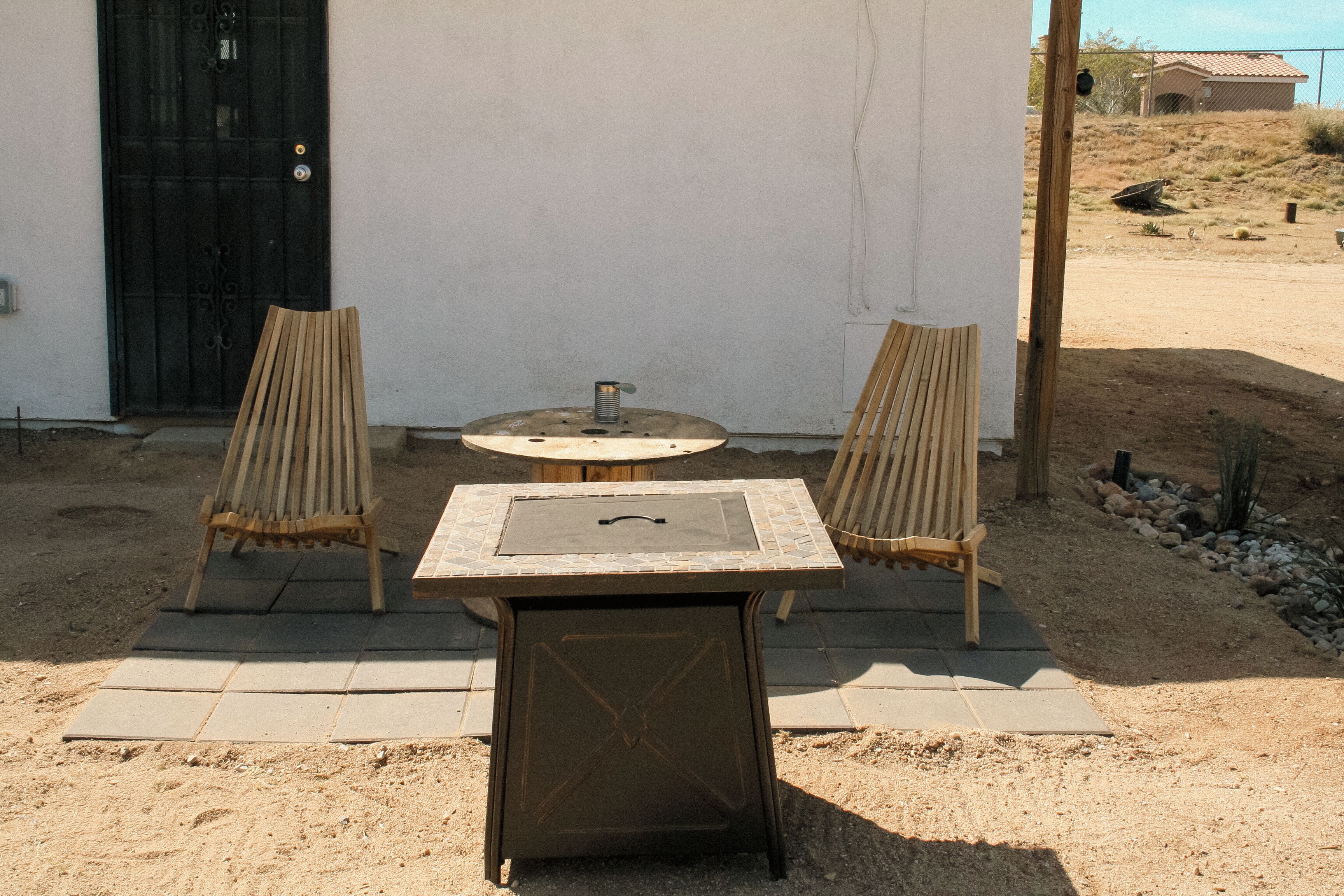 An outdoor seating area with a table and two chairs, a fire pit, and a black door.