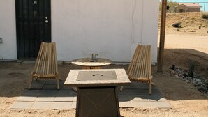 An outdoor seating area with a table and two chairs, a fire pit, and a black door. - A cozy 532 sq ft retreat in Yucca Valley, just minutes away from Joshua Tree NP (Yucca Valley)