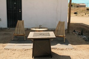 An outdoor seating area with a table and two chairs, a fire pit, and a black door. - A cozy 532 sq ft retreat in Yucca Valley, just minutes away from Joshua Tree NP (Yucca Valley)