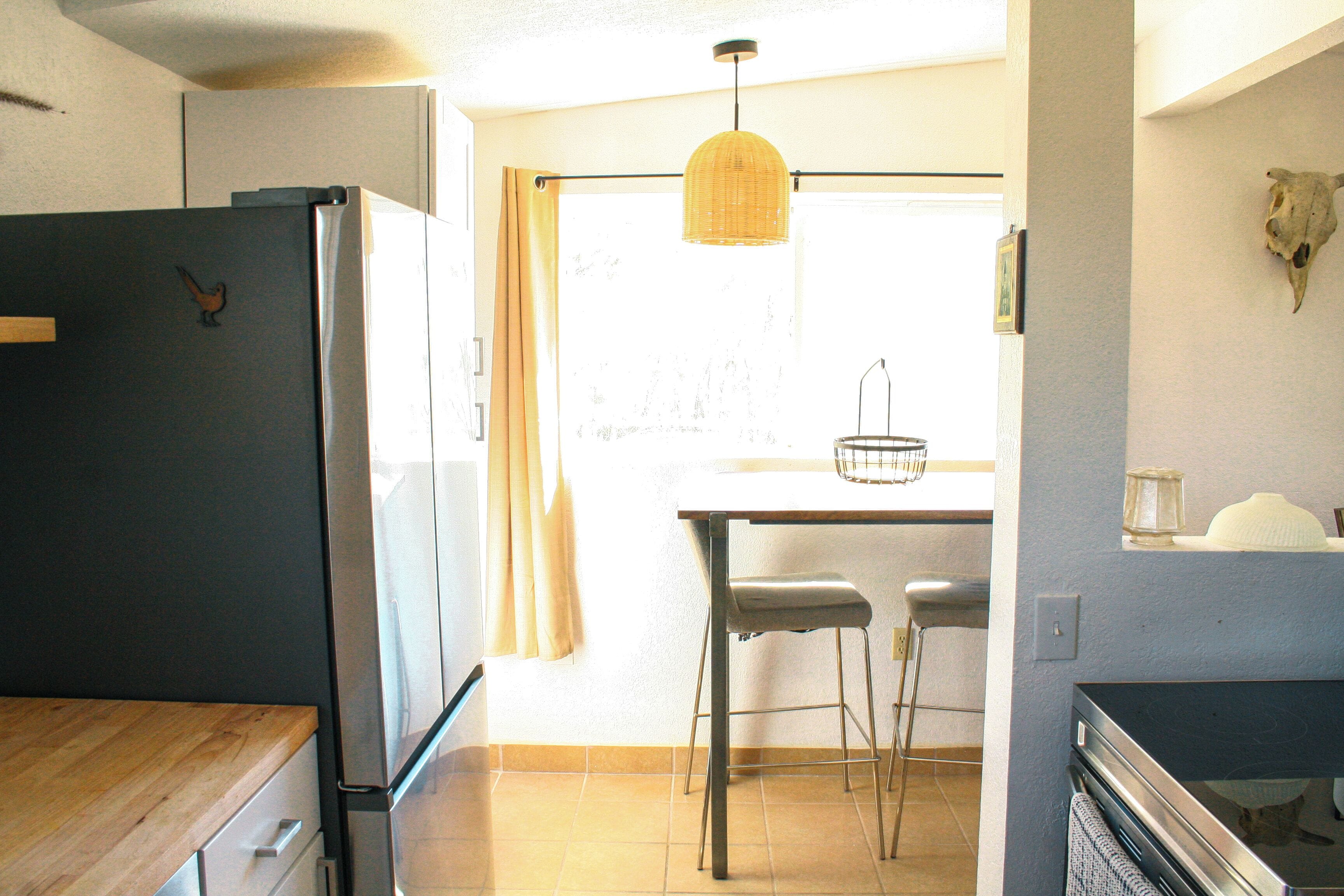 A kitchen with a refrigerator, wooden countertop, and a dining area with a table and chairs.