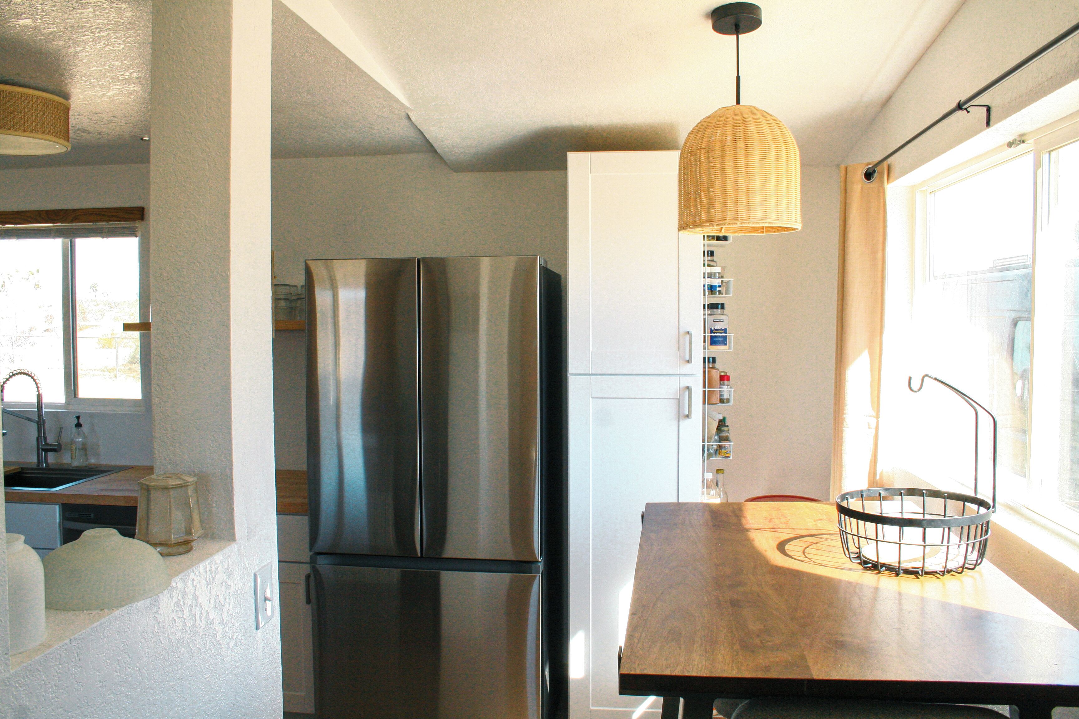 A kitchen with a stainless steel refrigerator, a wooden dining table, and a hanging light fixture.