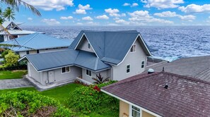 Une maison à deux étages avec un toit gris, un balcon et une vue sur l’océan.
