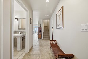 Un pasillo con un banco, una escalera y un baño con lavamanos y espejo.