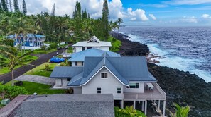A coastal property with a house featuring a prominent gable roof, a deck, and a view of the ocean. - *NEW* Pahoa Oceanfront Home for Sunrise and Rugged Coast Days (Pahoa)