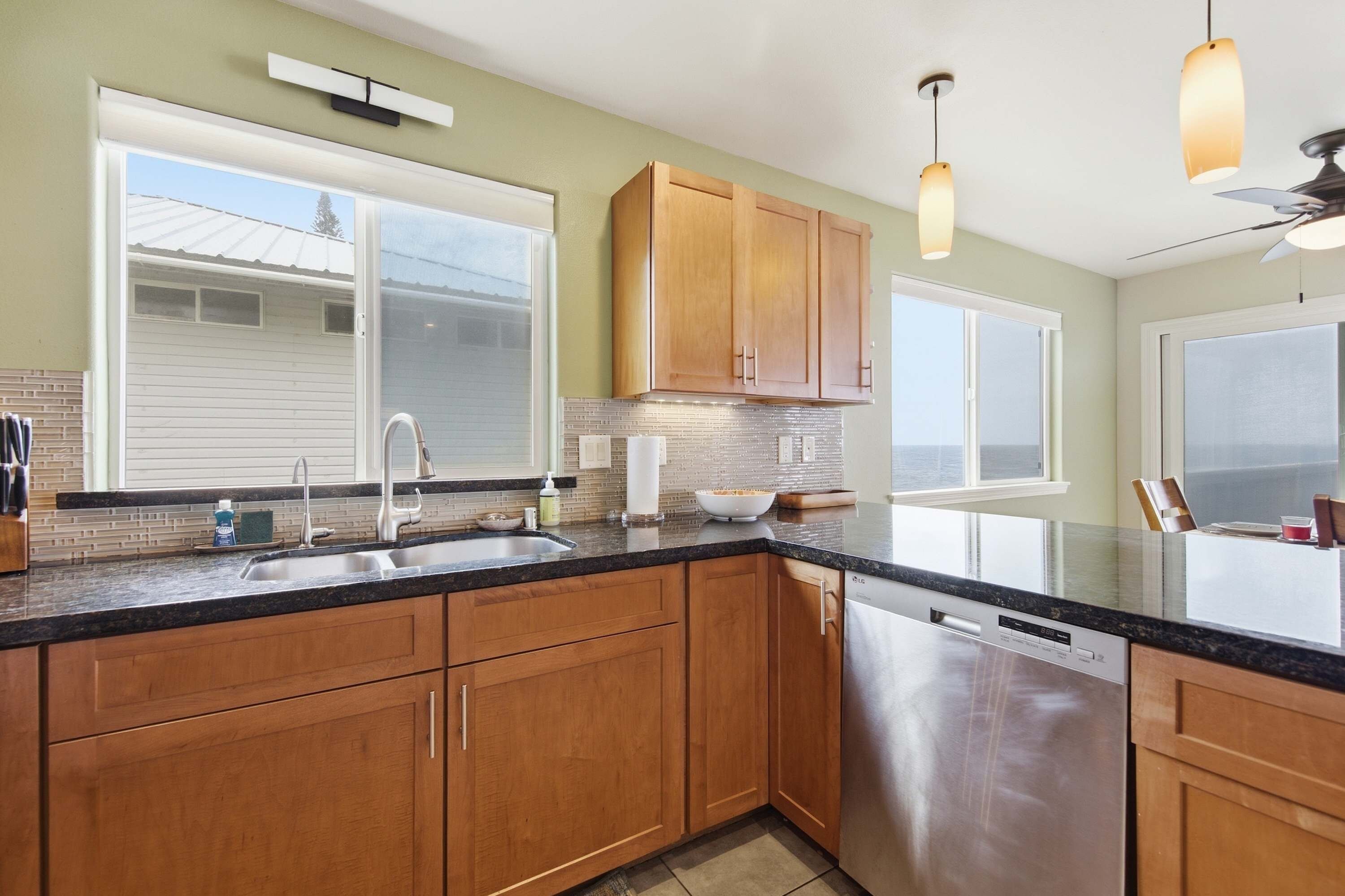 A kitchen with wooden cabinets, a stainless steel dishwasher, and a large window.