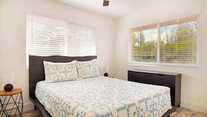 A bedroom with a bed, a nightstand, a dresser, a ceiling fan, and two windows with blinds. - New Dog-Friendly Pahoa Home with Yard, 31-Night Minimum (Pahoa)