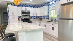 A modern kitchen with white cabinets, a large island with bar stools, a stainless steel refrigerator, and a microwave. - New Dog-Friendly Pahoa Home with Yard, 31-Night Minimum (Pahoa)