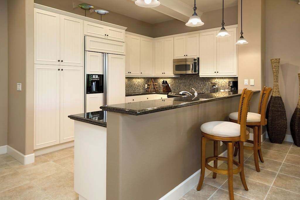 A kitchen with white cabinets, a central island with bar stools, a microwave, and a refrigerator.