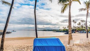 A beach with a covered table and chairs, palm trees, and a view of the sea. - NEW Mauna Lani Space, Pool Time, and Kohala Coast Sun (Waimea)