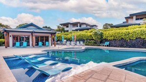 A swimming pool with lounge chairs, a covered area with umbrellas, and modern buildings in the background. - NEW Mauna Lani Space, Pool Time, and Kohala Coast Sun (Waimea)