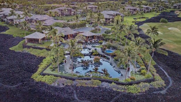Resort com várias edificações, área de piscina central e vegetação ao redor.