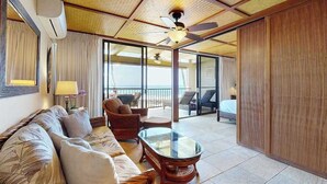 Ein Hotelzimmer mit Deckenventilator, einer Couch, einem Glastisch und Blick auf den Strand.