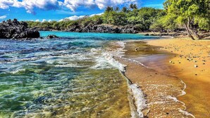 Ein Strand mit klarem Wasser, sandigem Ufer und einem Felsen.