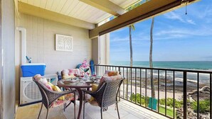 Ein Balkon mit Blick auf den Strand, einem Tisch mit Stühlen und einem Ventilator.