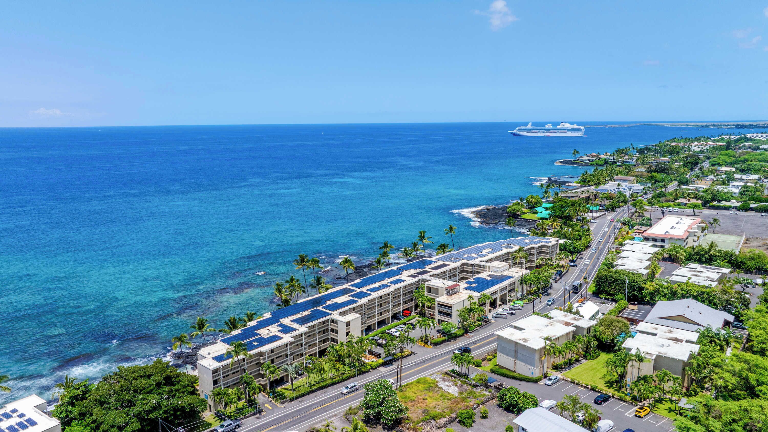 A coastal hotel with multiple buildings, a road, and a ship in the background.