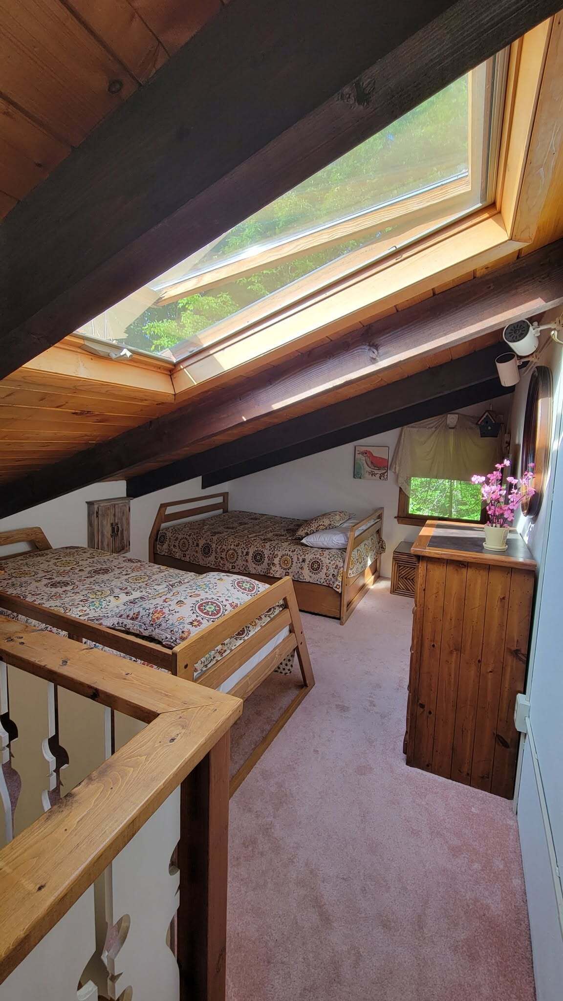 A cozy attic bedroom with a skylight, a bed, a sofa, a small desk, and a window with a view of greenery.