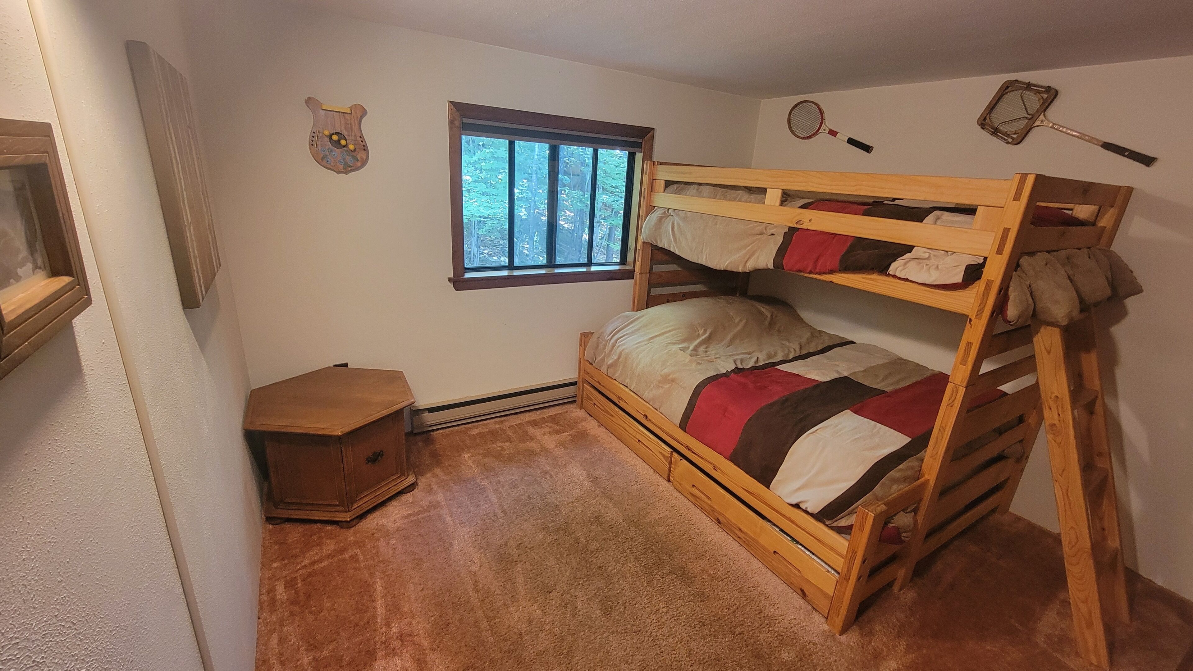 Une chambre avec un lit superposé, une fenêtre, une petite commode en bois et deux éléments fixés au mur.