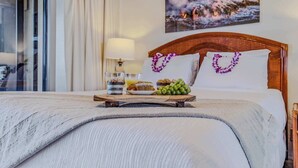 A hotel room with a bed, a tray with snacks, a painting of a waterfall, and a window with curtains. - NEW Fall Deal Wide Pacific Views from a Two-Bedroom Kona Condo (Kailua-Kona)