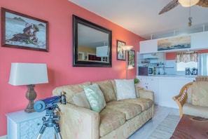 Ein Wohnzimmer mit einer Couch, einer Lampe, einem Teleskop und einer Küche im Hintergrund.