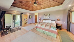 Ein Schlafzimmer mit einem Bett, einem Deckenventilator, einem Nachttisch, einer Bank und einer Glastür, die auf einen Balkon führt.