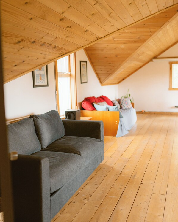 A loft-style room with a wooden floor, a grey sofa, and a red couch.
