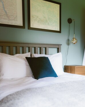 A bed with white bedding and a dark blue pillow, a wooden headboard, and a wall-mounted light fixture. - Rustic Lakefront Lodge on Little Atlin Lake - Pet friendly! (Tagish)