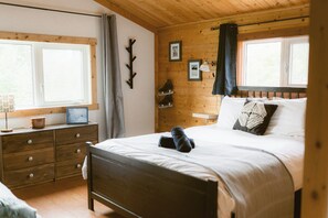 A wooden-paneled room with a bed, a dresser, a window, and a wall-mounted coat rack.