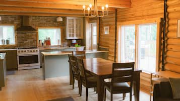 A wooden cabin interior with a kitchen, dining area, and large windows.