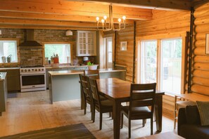 A wooden cabin interior with a kitchen, dining area, and large windows.