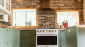 A kitchen with a brick wall, a window, and a stove. - Rustic Lakefront Lodge on Little Atlin Lake - Pet friendly! (Tagish)