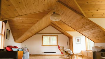 An attic room with wooden beams, a sloped ceiling, a window, a bed, a chair, and a radiator.