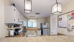 A kitchen with granite countertops, white cabinets, stainless steel appliances, pendant lights, and a window with a view. - *New* Fall Special Kona Family Condo Near Beach, Pool and Hot Tub (Kailua-Kona)