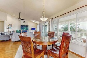 A spacious living area with a round wooden dining table, comfortable seating, a large window with a view, and a modern ceiling fan. - *NEW* Fall Special Mauna Kea Views and Family Space in Waimea (Waimea)
