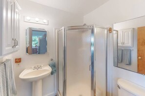 A bathroom with a glass shower enclosure, a sink, a mirror, and a cabinet.