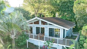 Une maison de plain-pied dotée d’un balcon, entourée d’une végétation luxuriante.