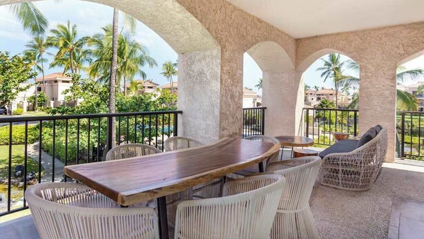 A covered outdoor seating area with a table and chairs, surrounded by arches and a view of palm trees and buildings. - *New* Fall Sale Renovated Waikoloa Condo Near A-Bay (Waikoloa)