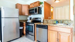 A compact kitchen with stainless steel appliances, wooden cabinets, and a granite countertop. - *New* Fall Sale Hilo Water-View Condo with Lanai, Pool, and Koi Stream (Hilo)