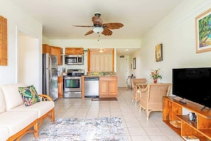 A modern kitchen with stainless steel appliances, a dining area with a TV, and a ceiling fan.