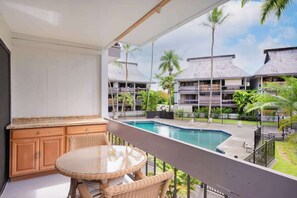 Ein Balkon mit Blick auf einen Swimmingpool, Holzmöbel und ein Gebäude mit mehreren Balkonen.