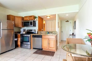 A compact kitchen with stainless steel appliances, wooden cabinets, and a glass dining table.