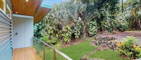 Una terraza de madera con barandilla metálica, un sendero de piedra y abundante vegetación.