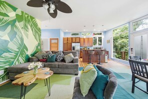 Ein modernes Wohnzimmer mit grauem Sofa, einem Couchtisch und einem Essbereich mit Holzschränken und einer Bar.