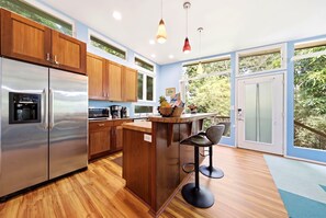 A modern kitchen with wooden cabinets, stainless steel appliances, and a bar area with stools. - Tranquil Island Escape at Kehena Beach - Private Home at Black Sands and Volcano (Pahoa)